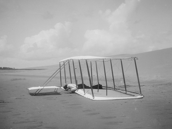 글라이더가 모래사장에 착륙한 직후 모습. 조종사 윌버 라이트가 복엽기 아래날개에 바짝 엎드린 자세를 취하고 있다(1901년, 노스 캐롤라이나 키티 호크 해변). <br>